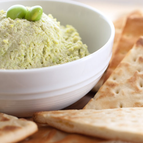 edamame hummus in white bowl with pita chips.