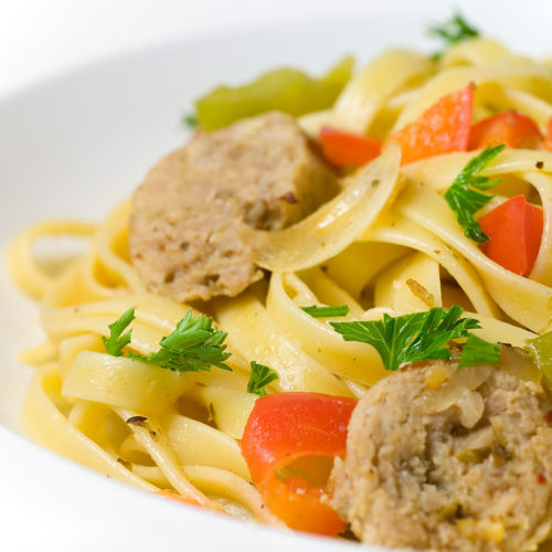 Fettuccini with sausage peppers and onions in white bowl.