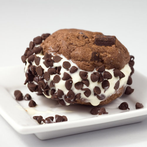 fudgy brownie cookie ice cream sandwich on white plate.