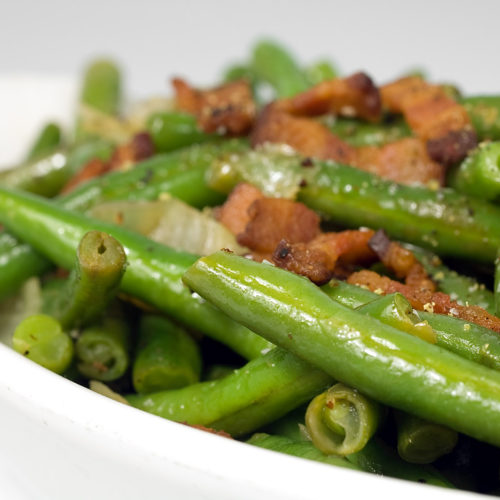 Close up of green beans with pepper bacon in white dish.