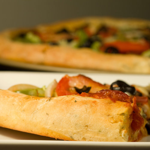 Slice of pizza on white plate with crust facing forward.