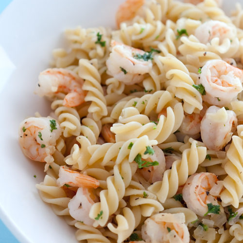 Lemon pepper shrimp fusilli in white bowl with blue background.