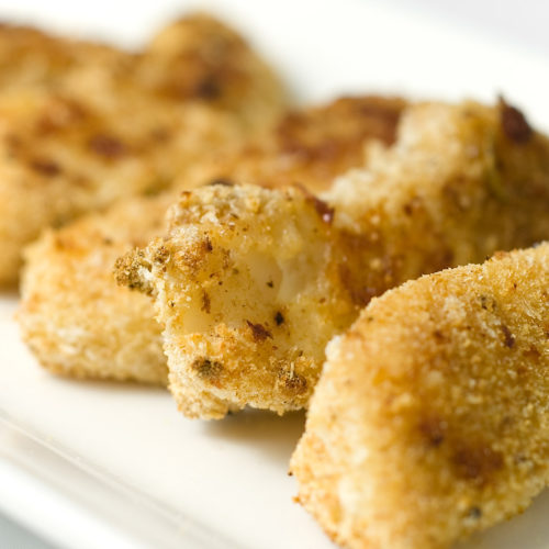 close up of oven baked fish sticks on white plate.