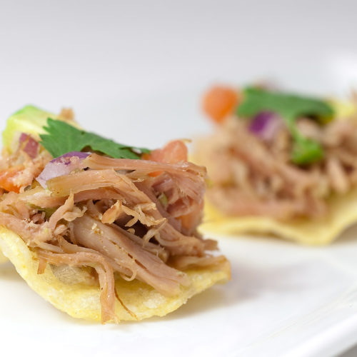 pulled pork on potato chips on white plate.