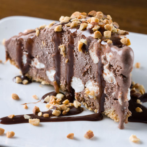 Slice of rocky road ice cream pie with chocolate drizzle.