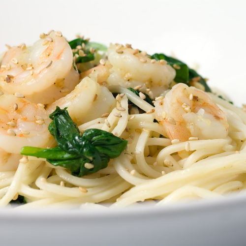 Sesame shrimp and spinach noodles in white bowl.