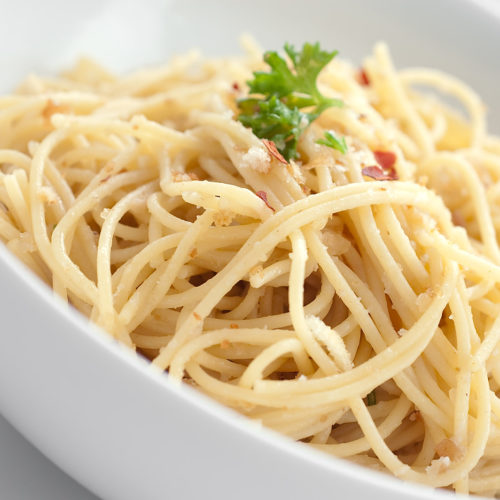 Close up of spaghetti with bread crumbs and anchovies in white bowl.