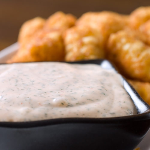 Sriracha ranch dip in square bowl with tater tots.