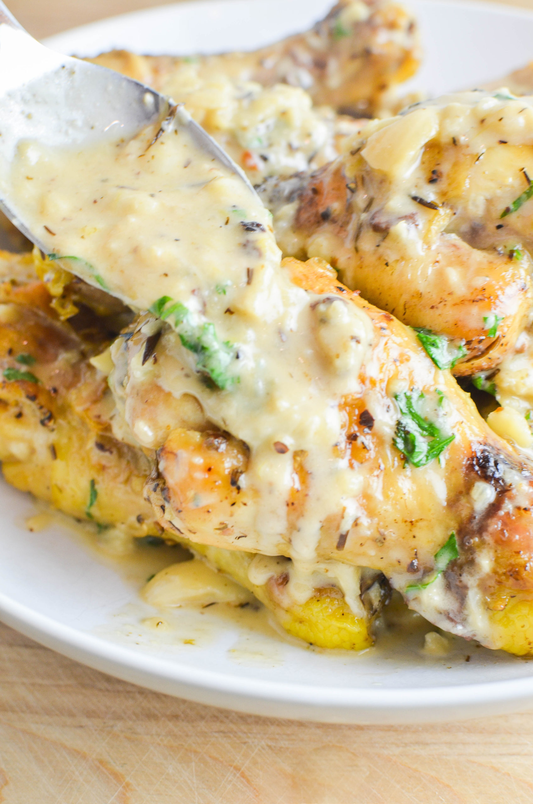 Pouring garlic sauce over chicken on a white plate. 