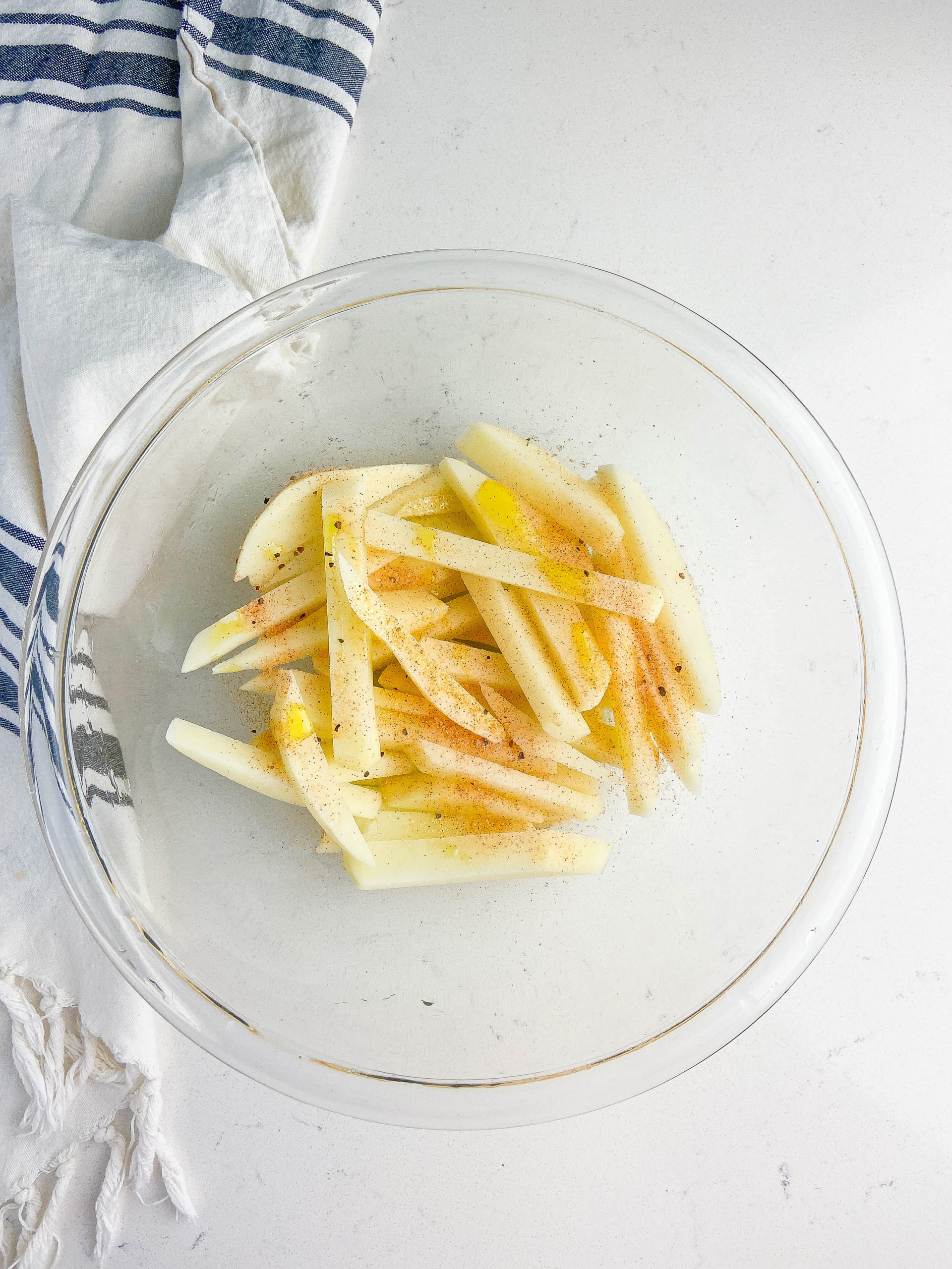 French fries in a clear glass bowl with oil and seasoning salt. 