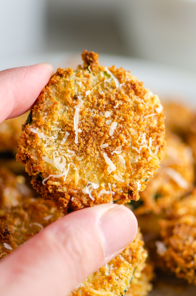 Hand holding fried zucchini chip.