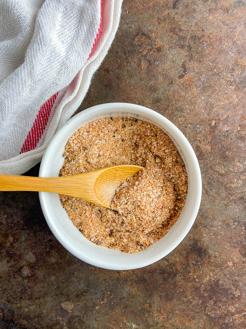 All purpose seasoning blend in a white bowl on cookie sheet with white and red stripped towel.