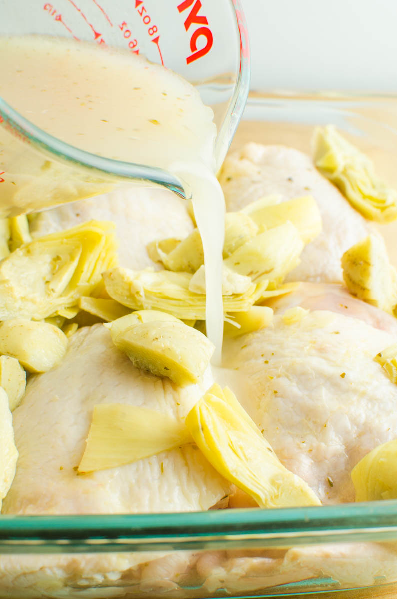 Pouring artichoke marinade over chicken in a glass dish. 