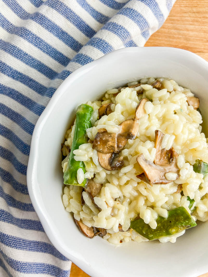 Asparagus and Mushroom Risotto in a white bowl with a striped blue towel on a cutting board.