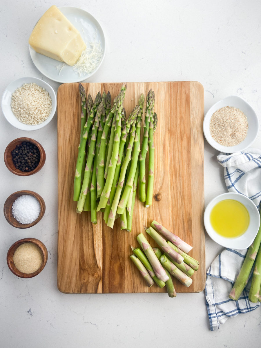 Asparagus with ends snapped off on wooden cutting board. 