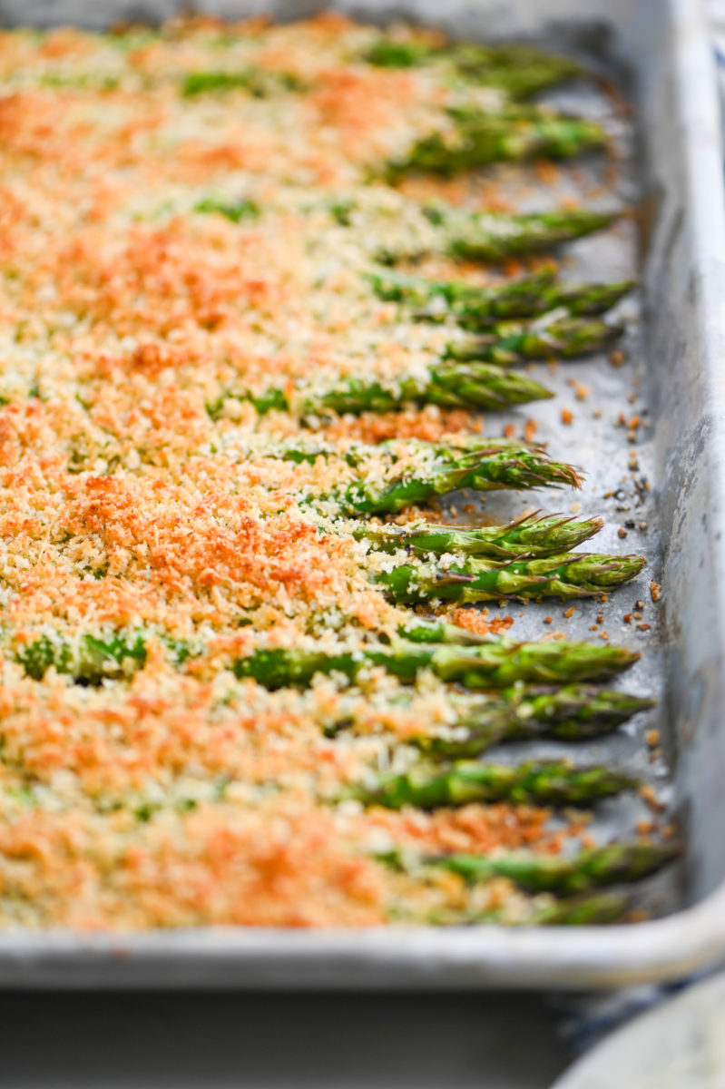 Asparagus on baking dish covered with breadcrumbs.