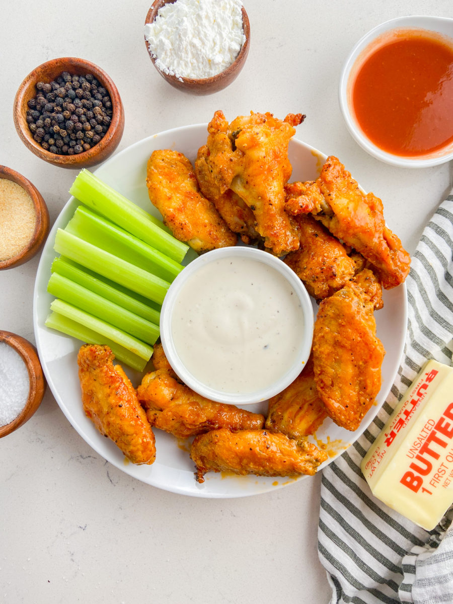Buffalo wings on white plate with ranch dressing and celery. 