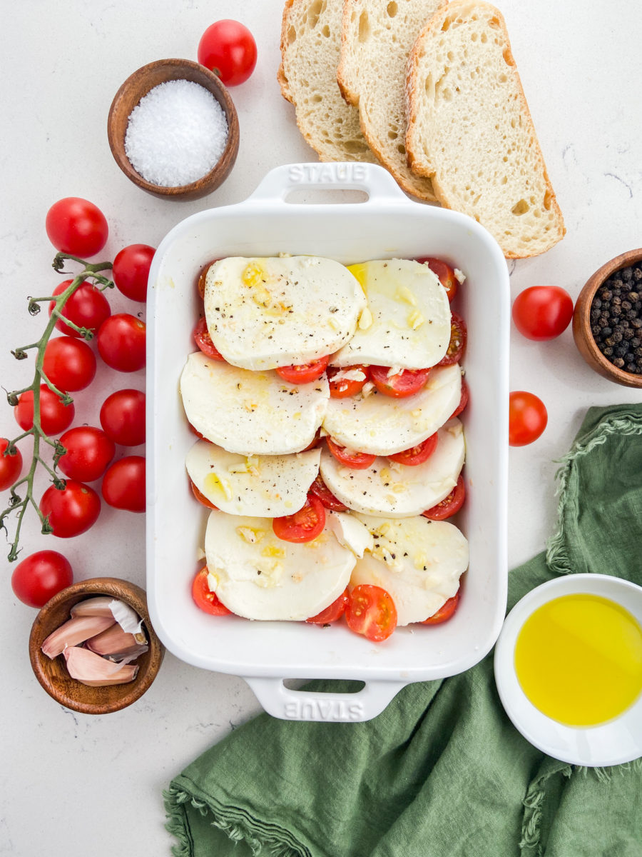 Overhead photo of mozzarella layered with tomatoes in white baking dish. 