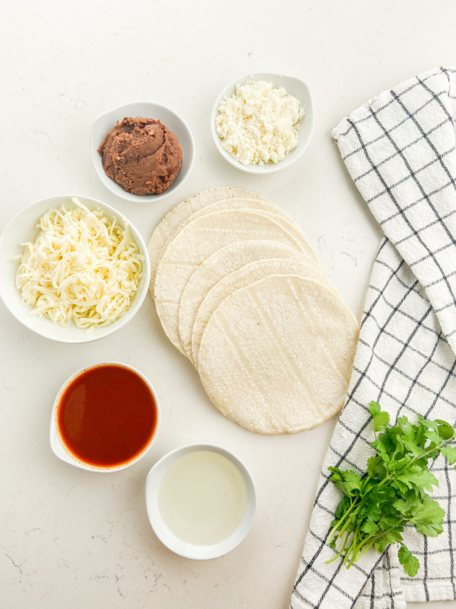Overhead photo of ingredients for bean and cheese enchiladas on white background. 