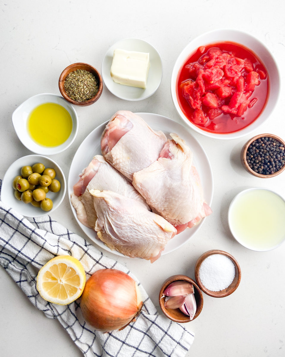 Overhead photo of ingredients for braised chicken with tomatoes and olives on white background. 