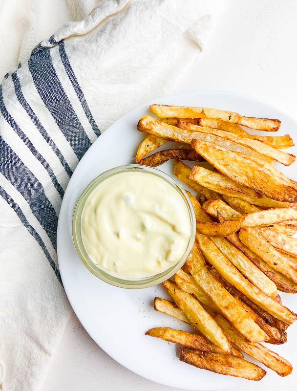 French fry dip in a bowl on a white plate with french fries and a striped towel. 
