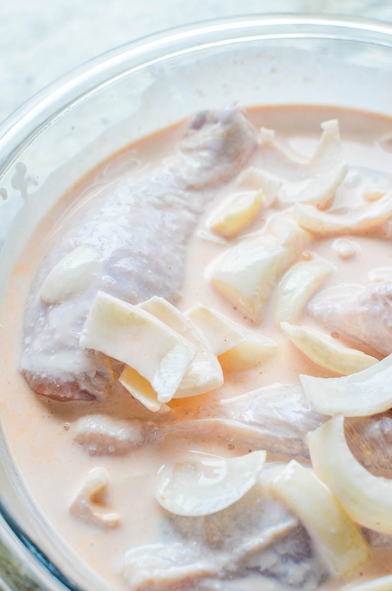 Chicken Marinating in a bowl with buttermilk, onions and garlic. 