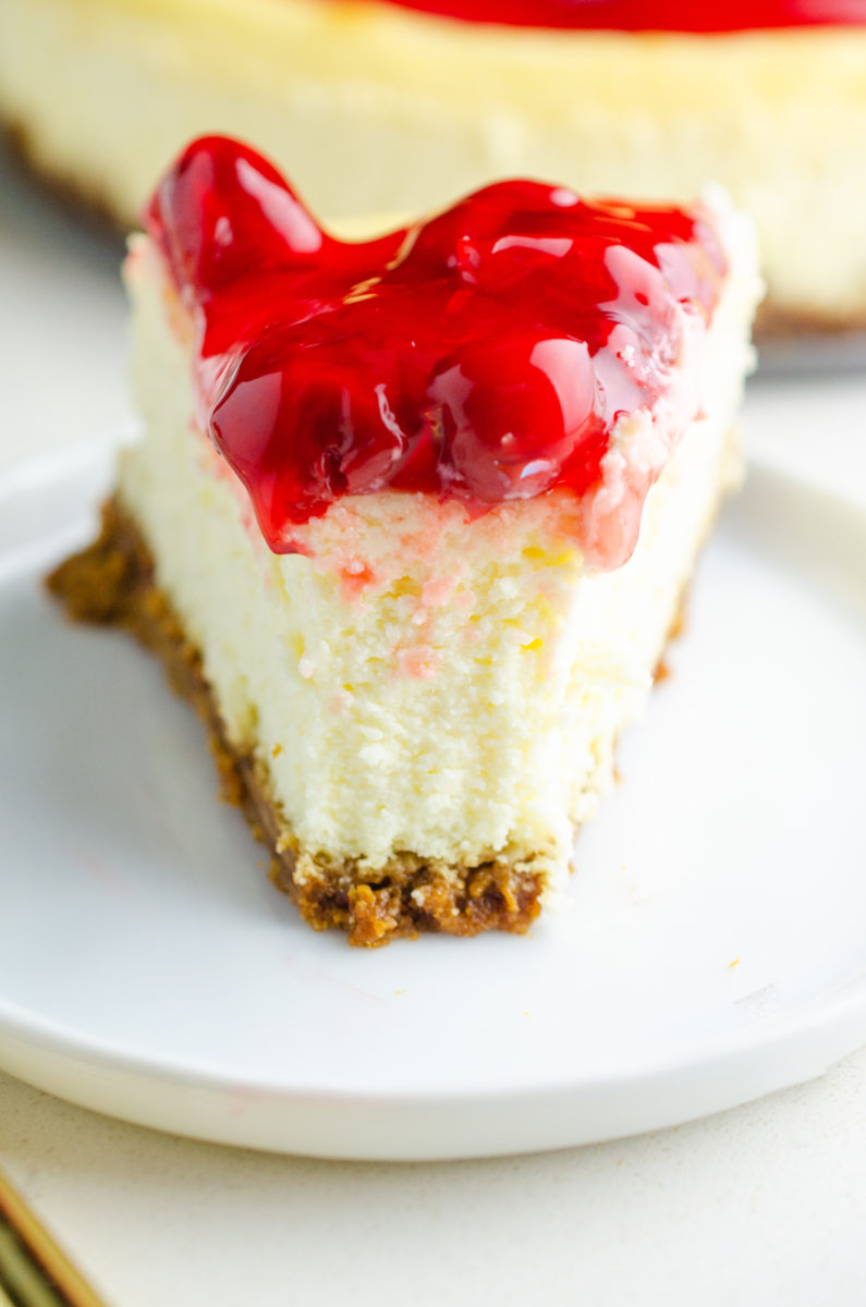 Cherry cheesecake on a plate with a bite missing. 