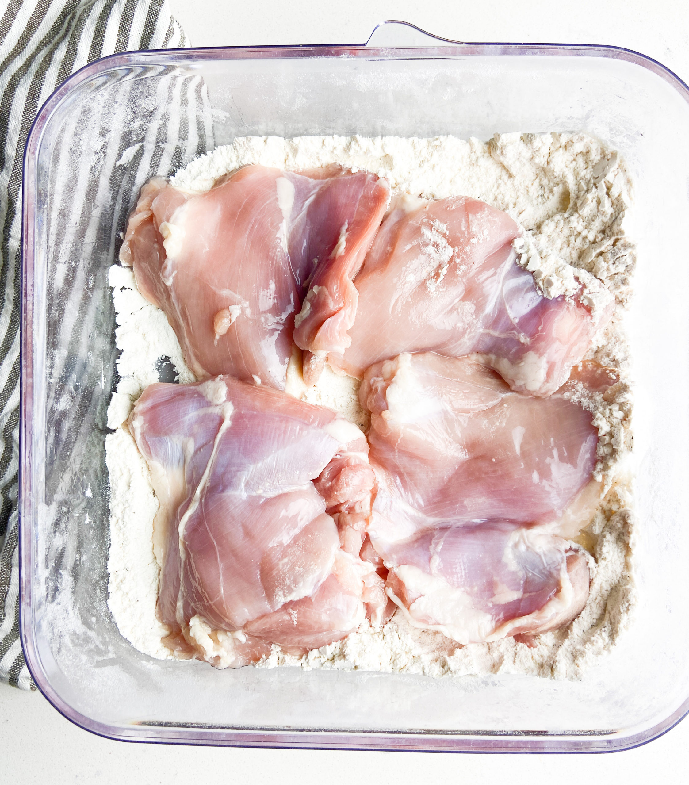 Boneless skinless chicken thighs in a shallow dish with flour. 