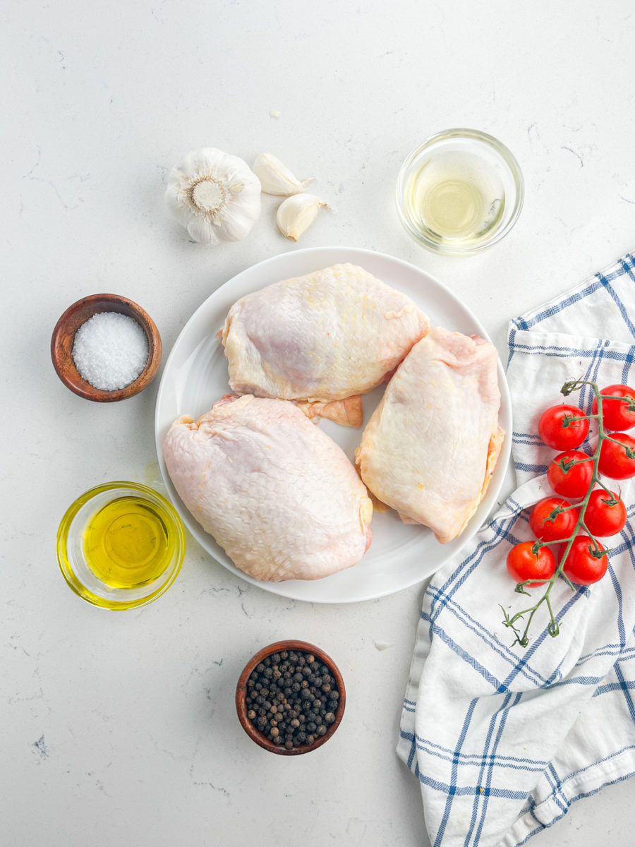 Raw chicken thighs on a white plate with cherry tomatoes on white background. 