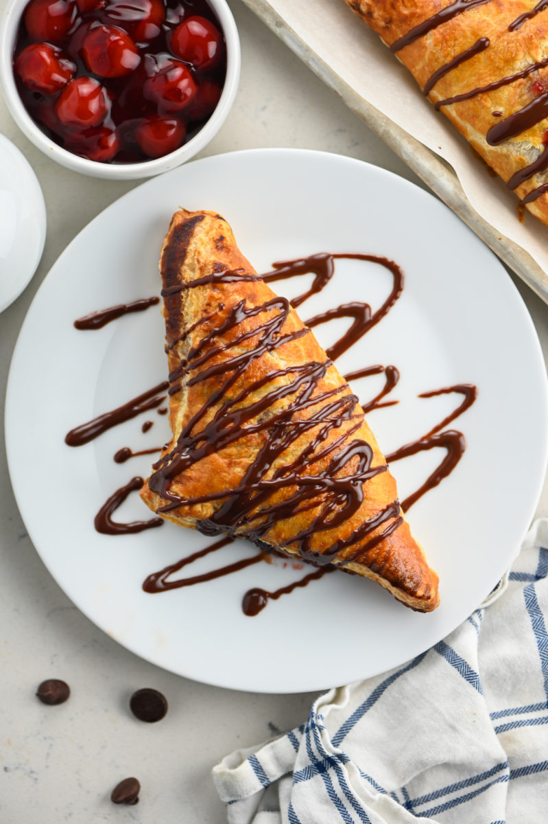 chocolate cherry turnover on white plate with ganache drizzled over the top. 