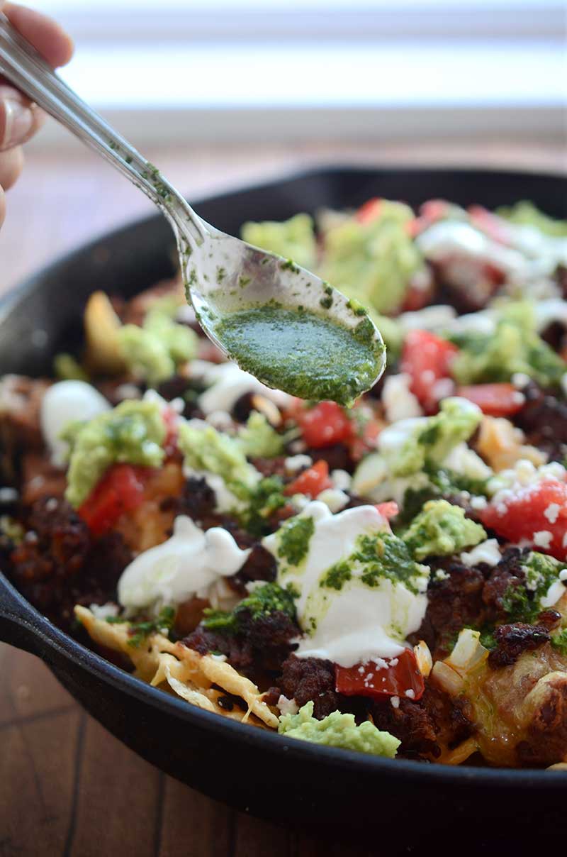 Chorizo Skillet Nachos are fully loaded with chips, refried beans, cheese, chorizo, guacamole, sour cream, onions, tomatoes and Habanero Chimichurri.