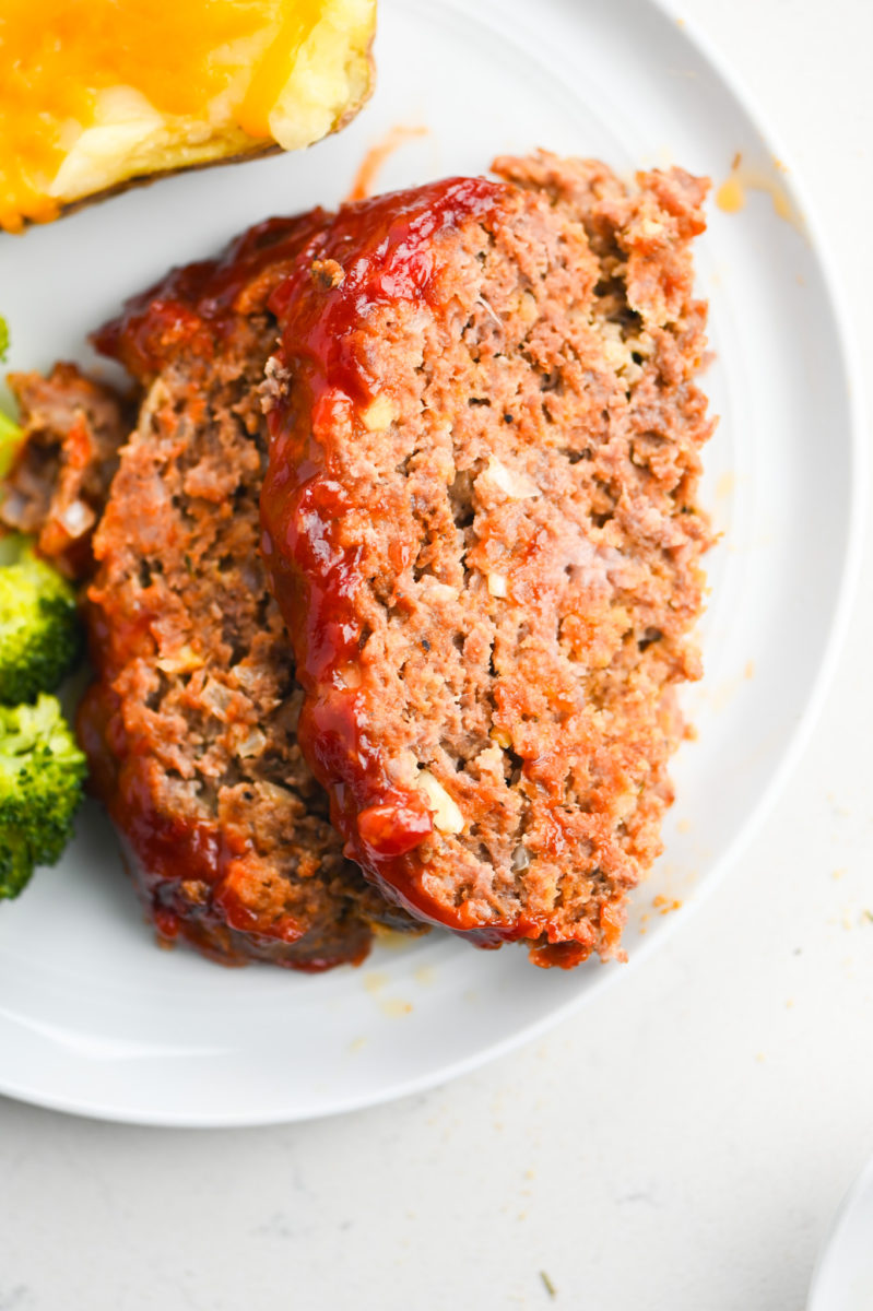 Classic meatloaf recipe on white plate with broccoli. 