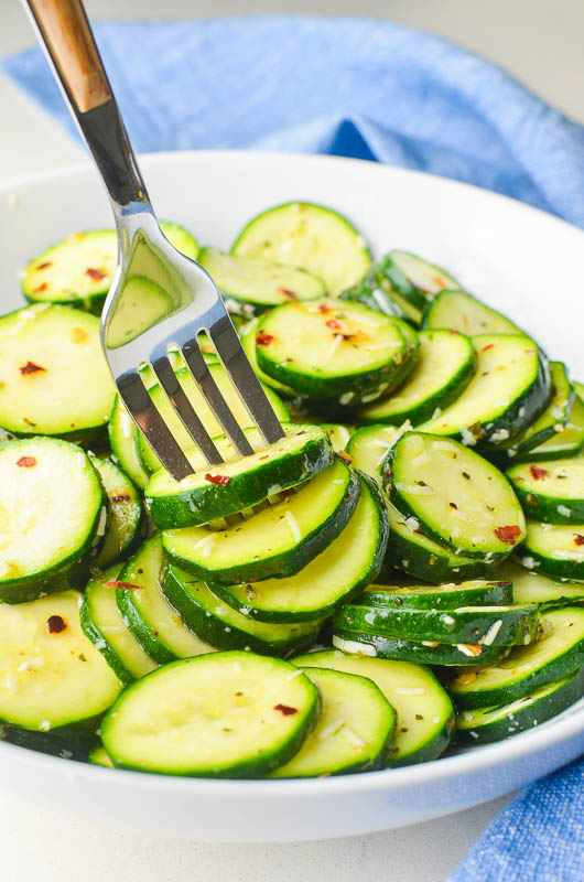 Zucchini salad on a fork in a white bowl with blue napkin. 