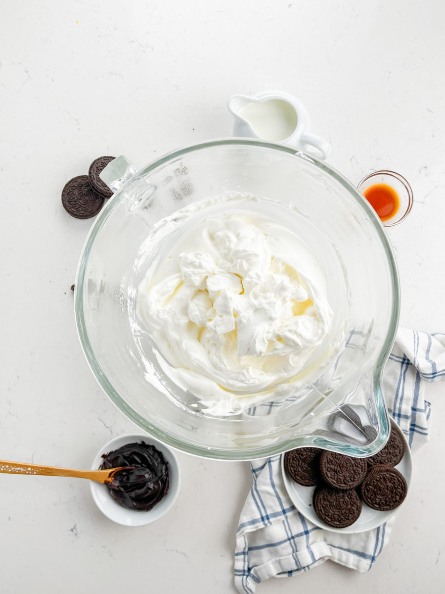 Whipped cream in a glass bowl of stand mixer. 