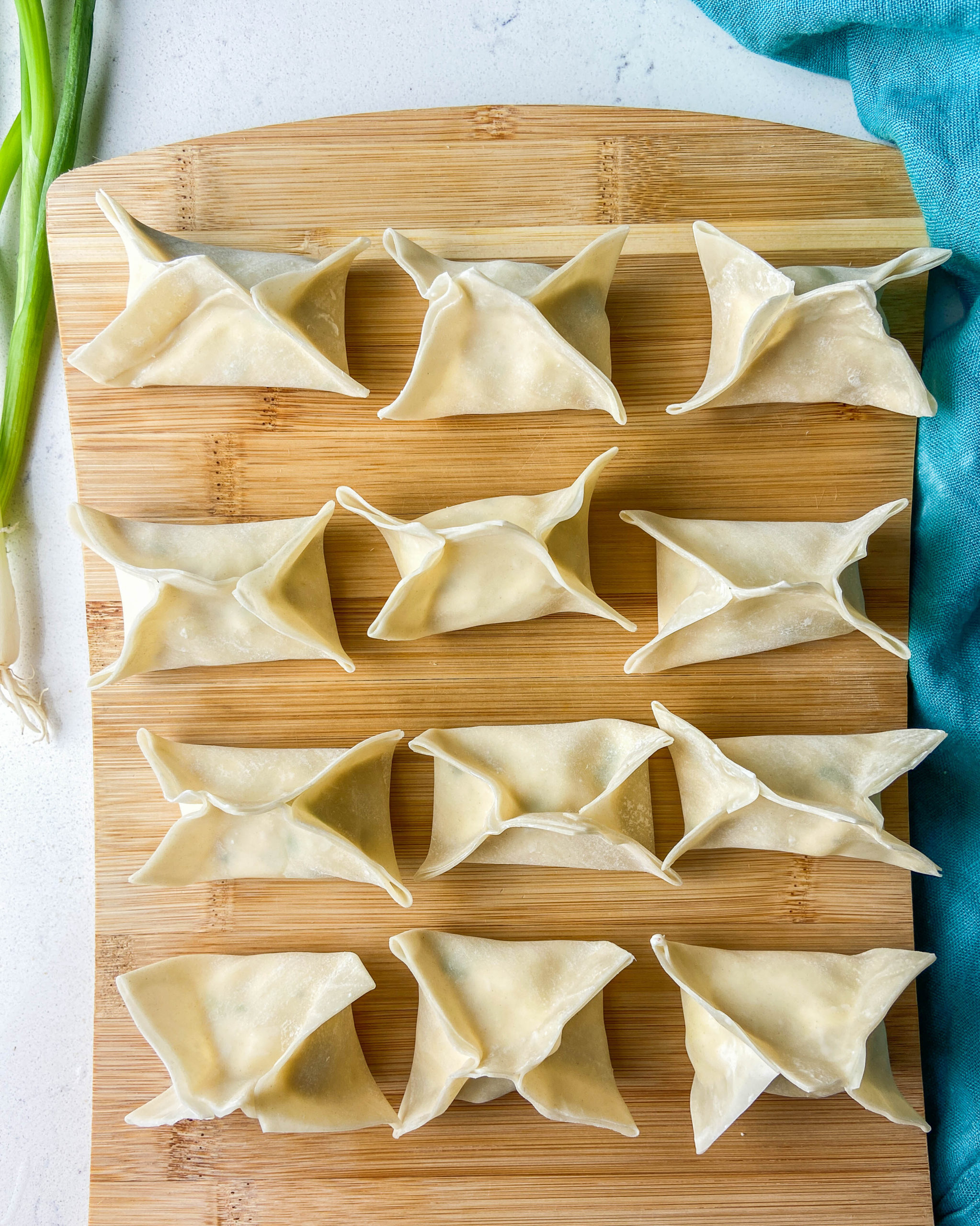 Overhead photo of uncooked wontons on a wooden cutting board. 