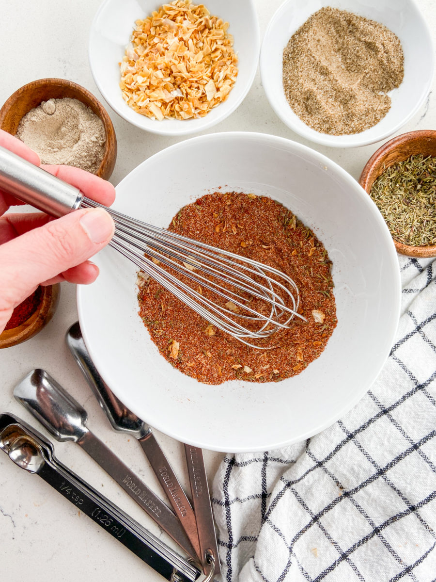 Whisking together cajun seasoning ingredients in white bowl. 