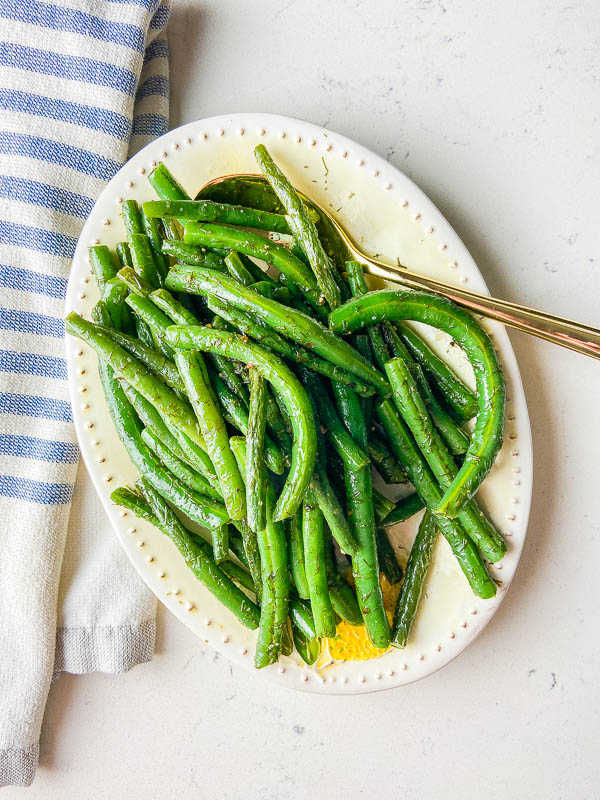 Overhead photo of green beans on an oval plate. White background and blue striped towel. 