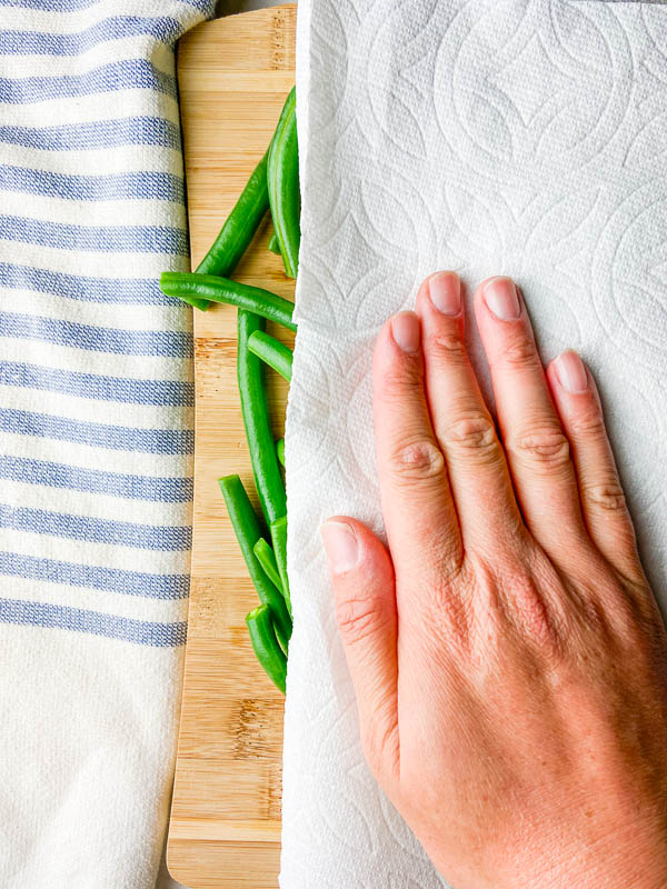 Patting green beans dry with a paper towel. 