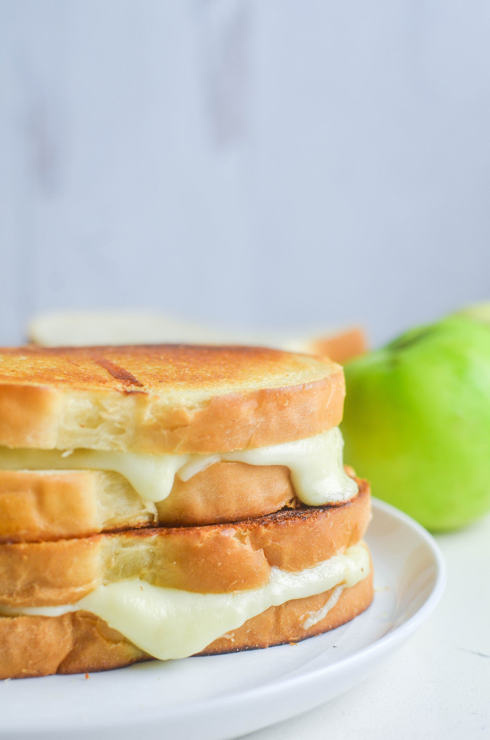 Two fried green tomato sandwiches stacked on top of each other on a white plate with a green tomato in the background.