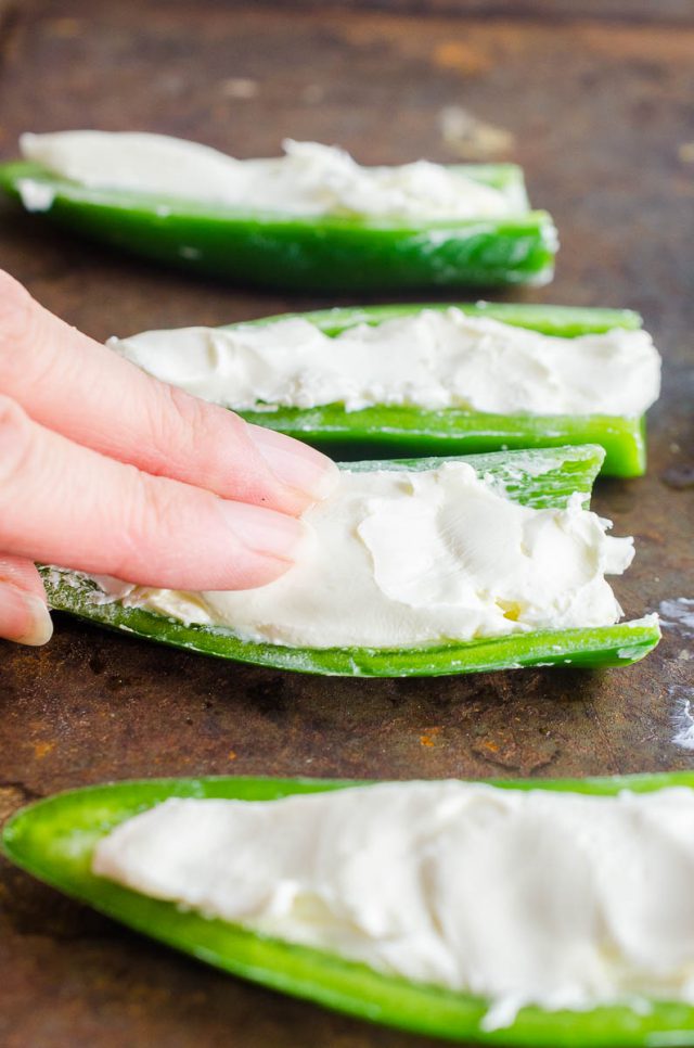 Pressing cream cheese into jalapeno. 