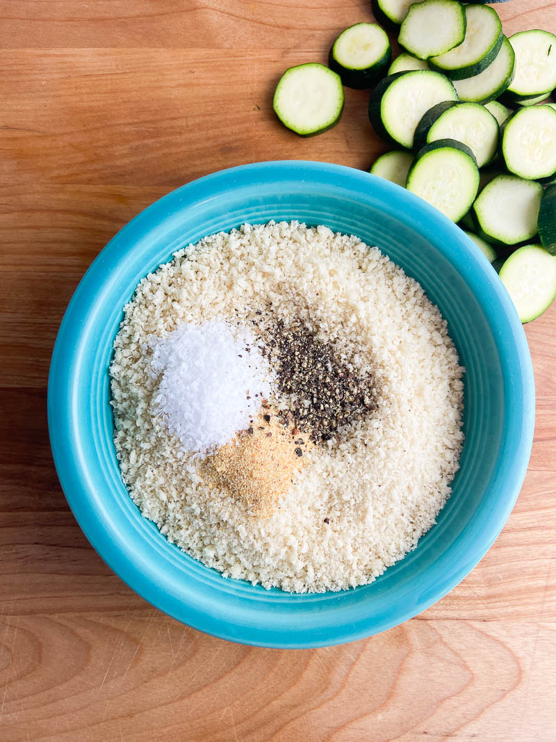 Seasoned panko bread crumbs in a teal bowl on a wooden cutting board. 