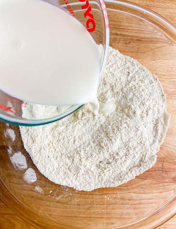 Pouring milk into dry ingredients in a clear bowl. 