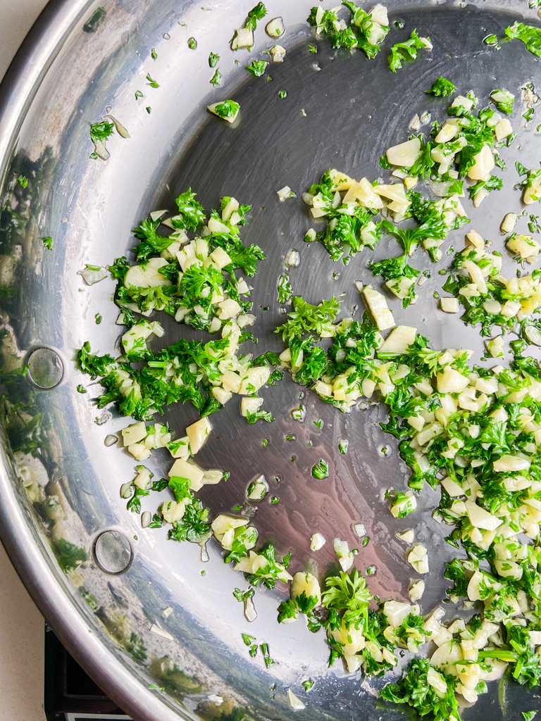 Garlic and parsley cooking in stainless steel pan. 
