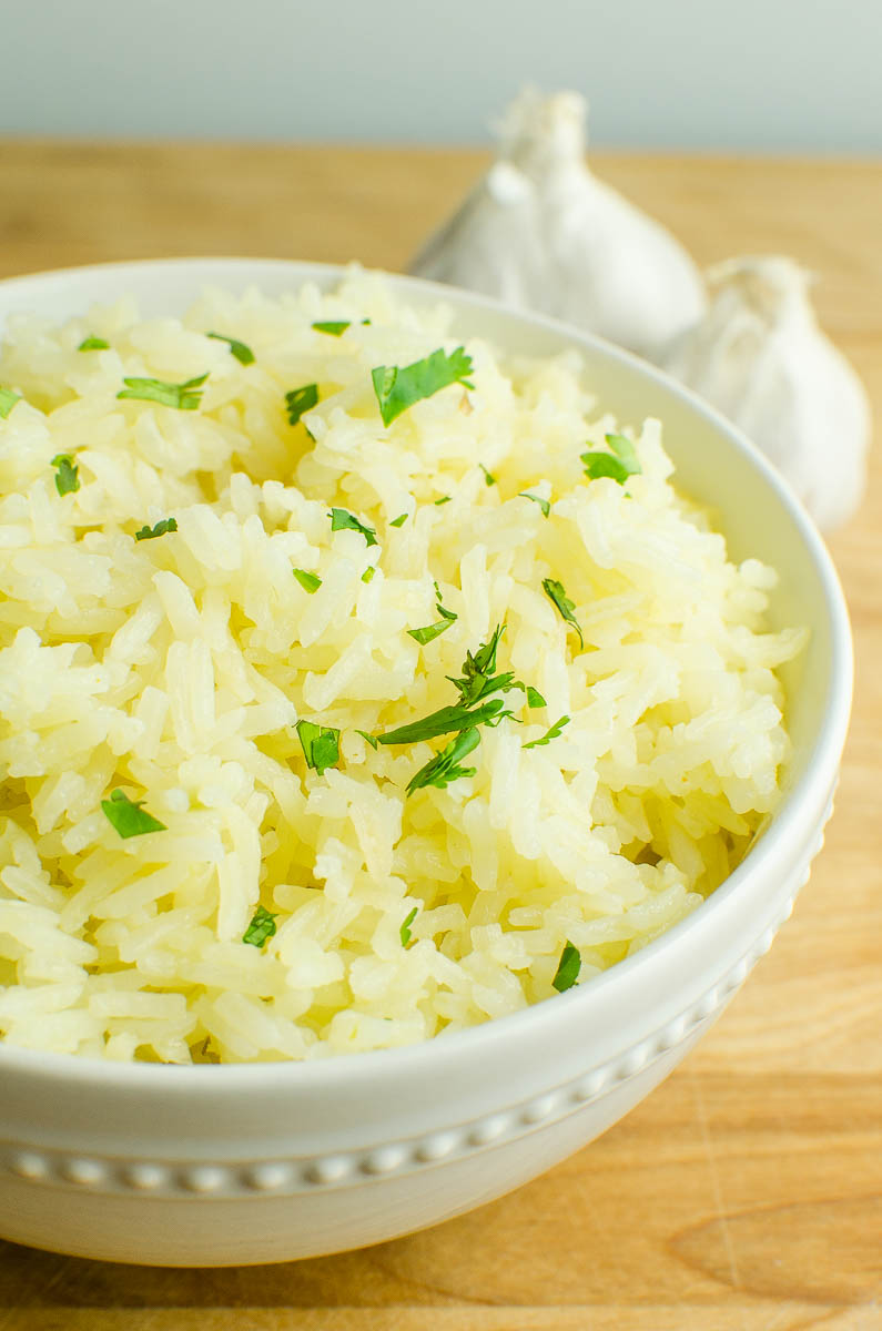 Garlic rice in a white bowl on a wooden cutting board. 