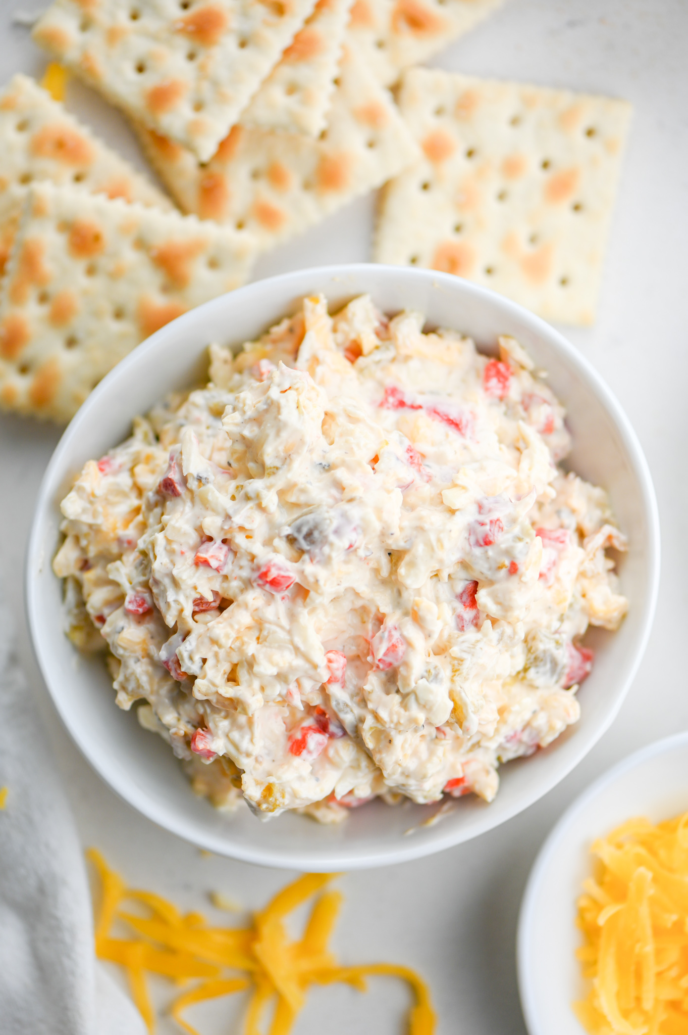 Overhead photo of green chile pimento cheese in a white bowl with saltine crackers. 