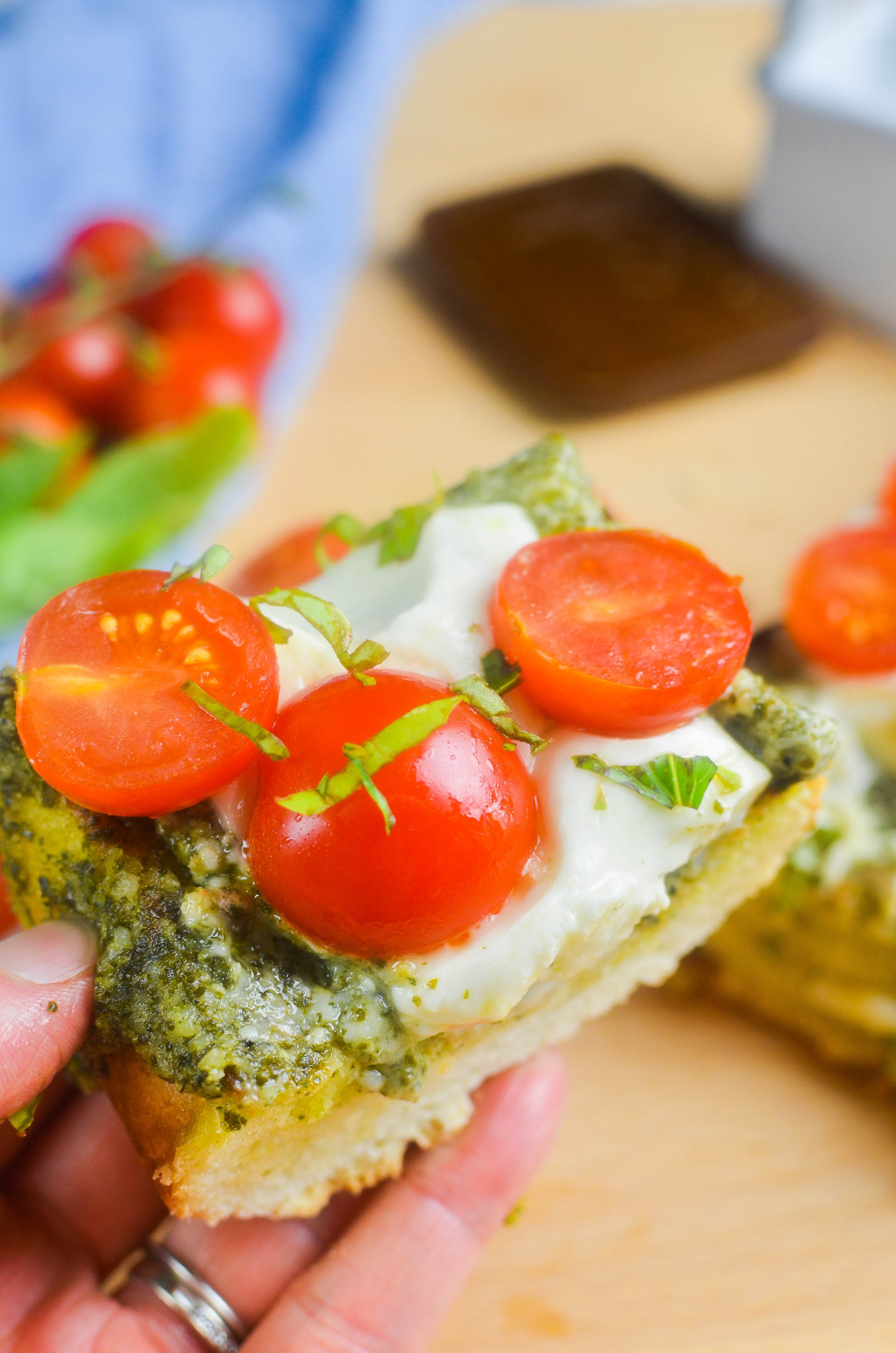 Hand holding a slice of caprese burrata cheese bread. 