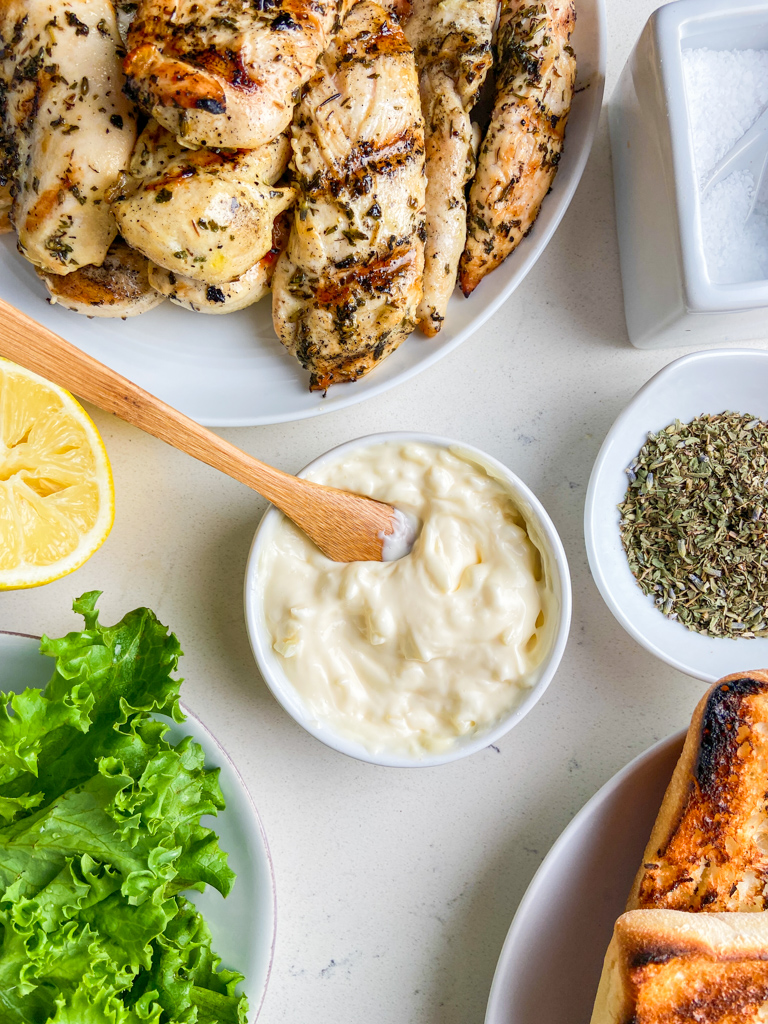 Overhead photo of garlic mayonnaise in a white bowl with a wooden spoon. 