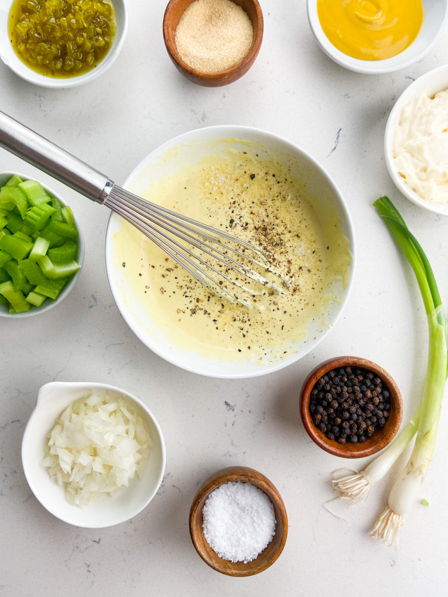 Potato salad dressing in white bowl with whisk. 