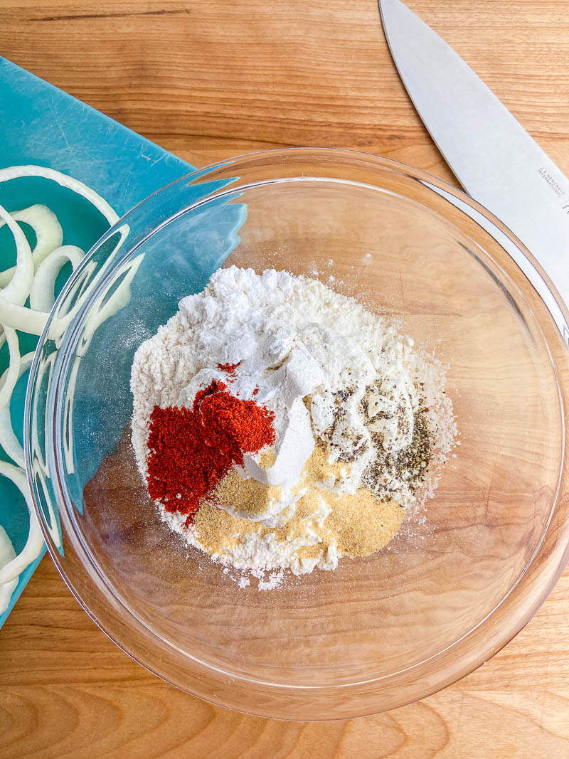 A bowl of seasoned flour on a wooden cutting board. 