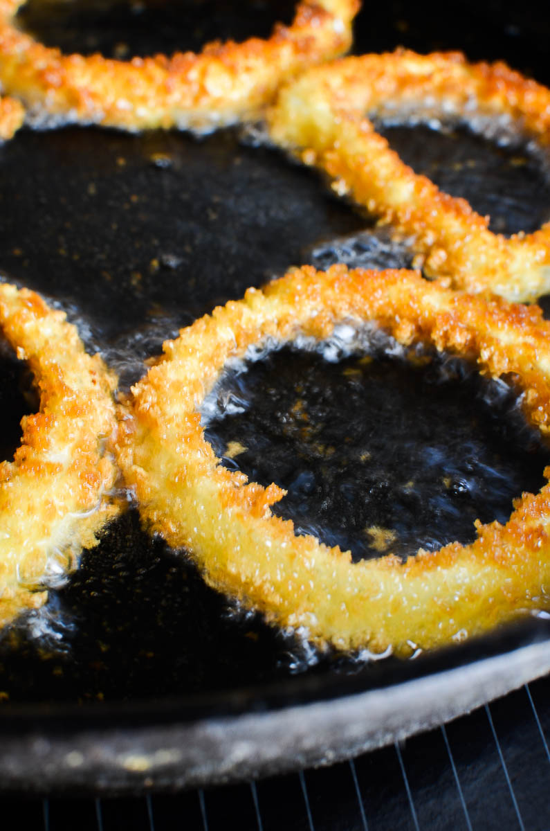Onion rings frying in a cast iron skillet. 